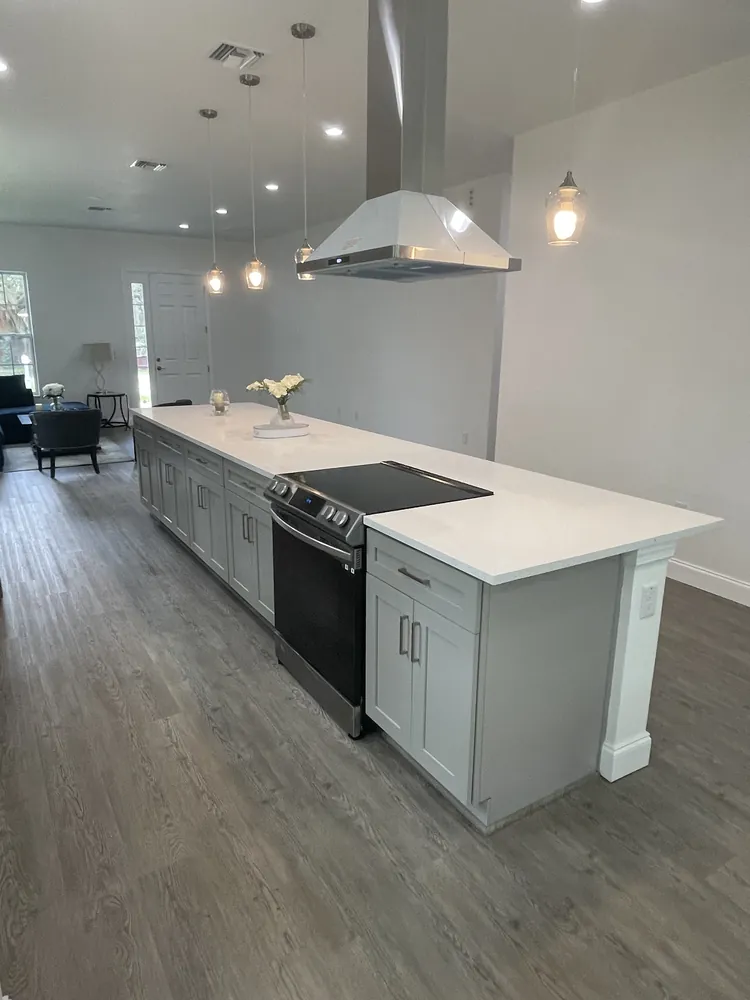 Kitchen with a grey island, pendant lights and a stainless range hood