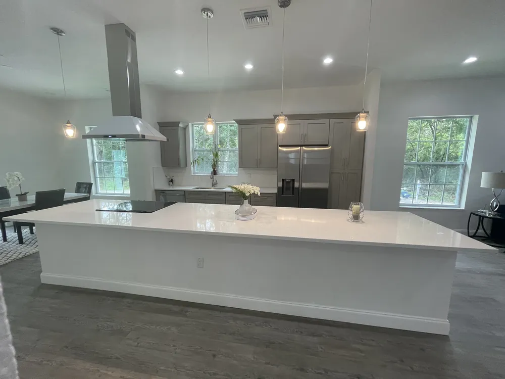 Wide view of a remodeled kitchen with a grey island, pendant lights and stainless hood